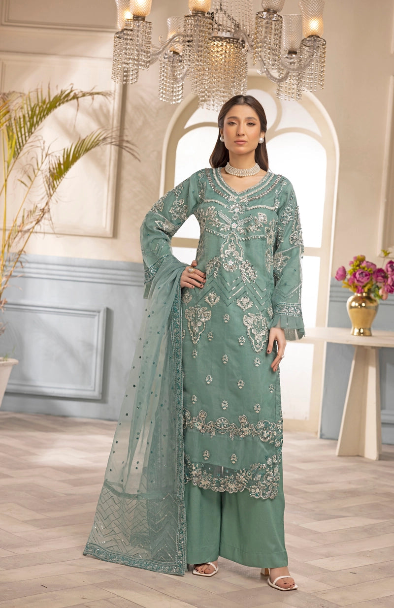 Woman in a green embroidered outfit standing in a decorated room with a chandelier.