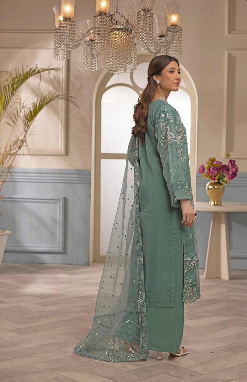 Woman in a green embroidered outfit standing in an elegant room with chandeliers and decor.