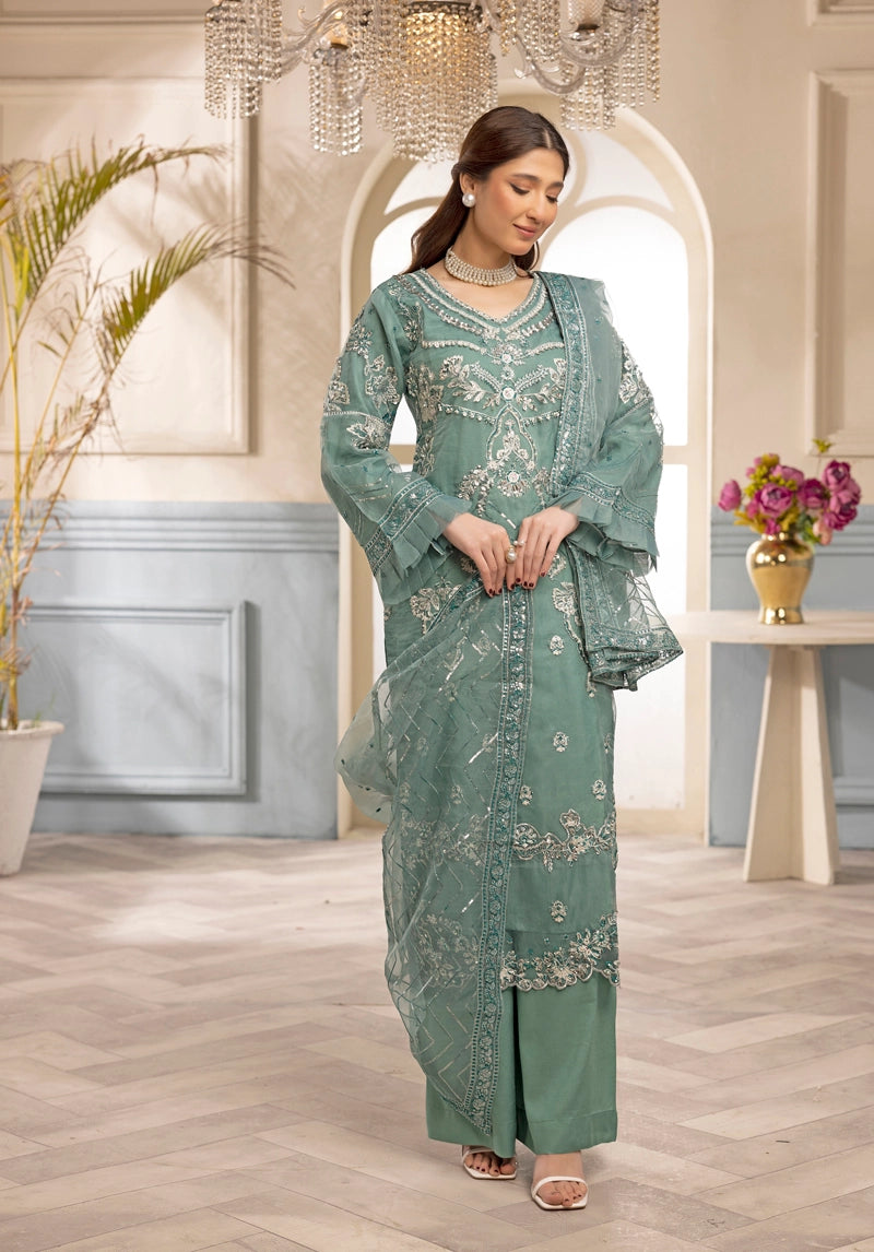Woman in a green embroidered traditional outfit standing in an elegant room with chandeliers and a vase.