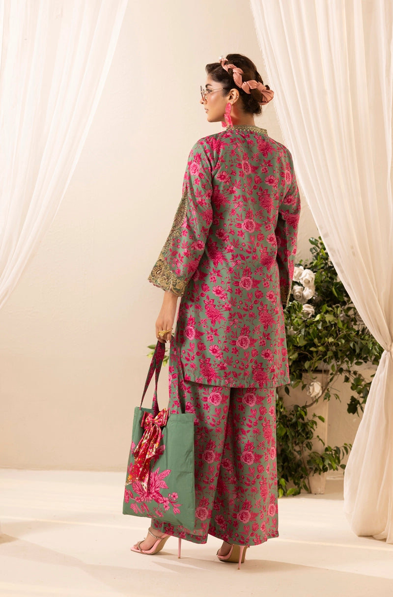 Woman wearing a floral outfit with a green bag, standing in front of white curtains and plants.