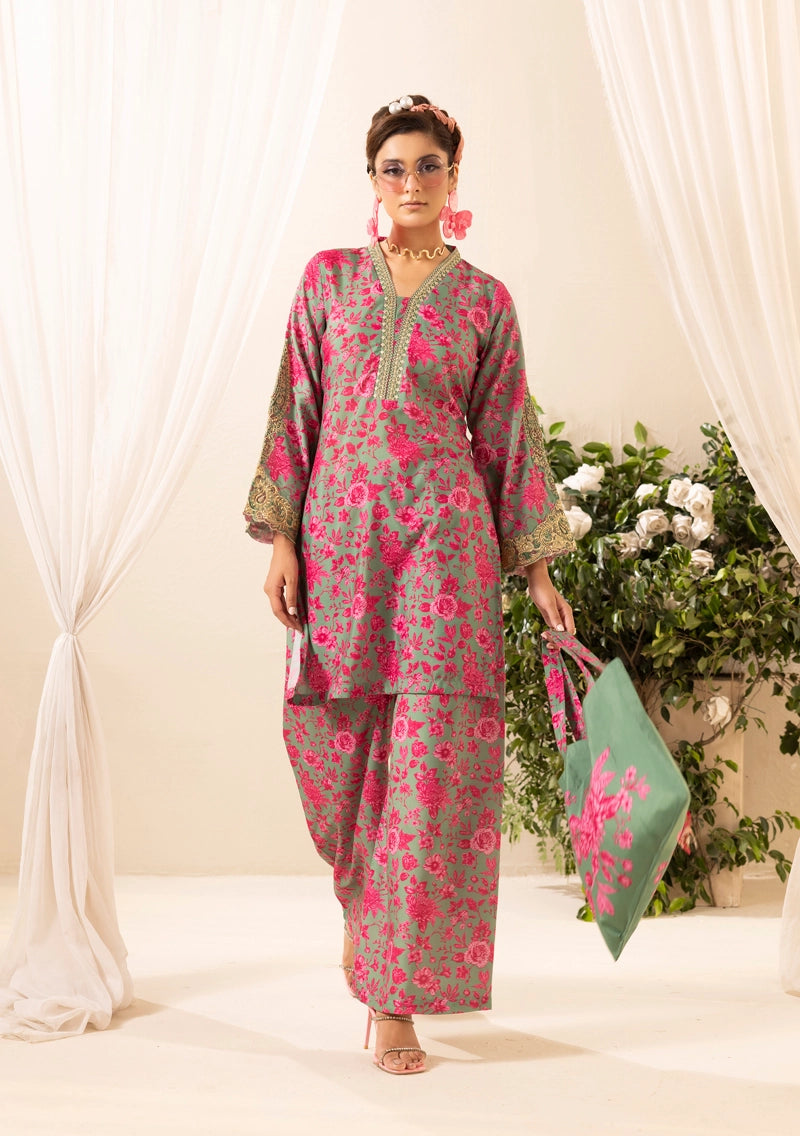 Woman in a floral outfit holding a green bag with pink flowers against a white curtain background