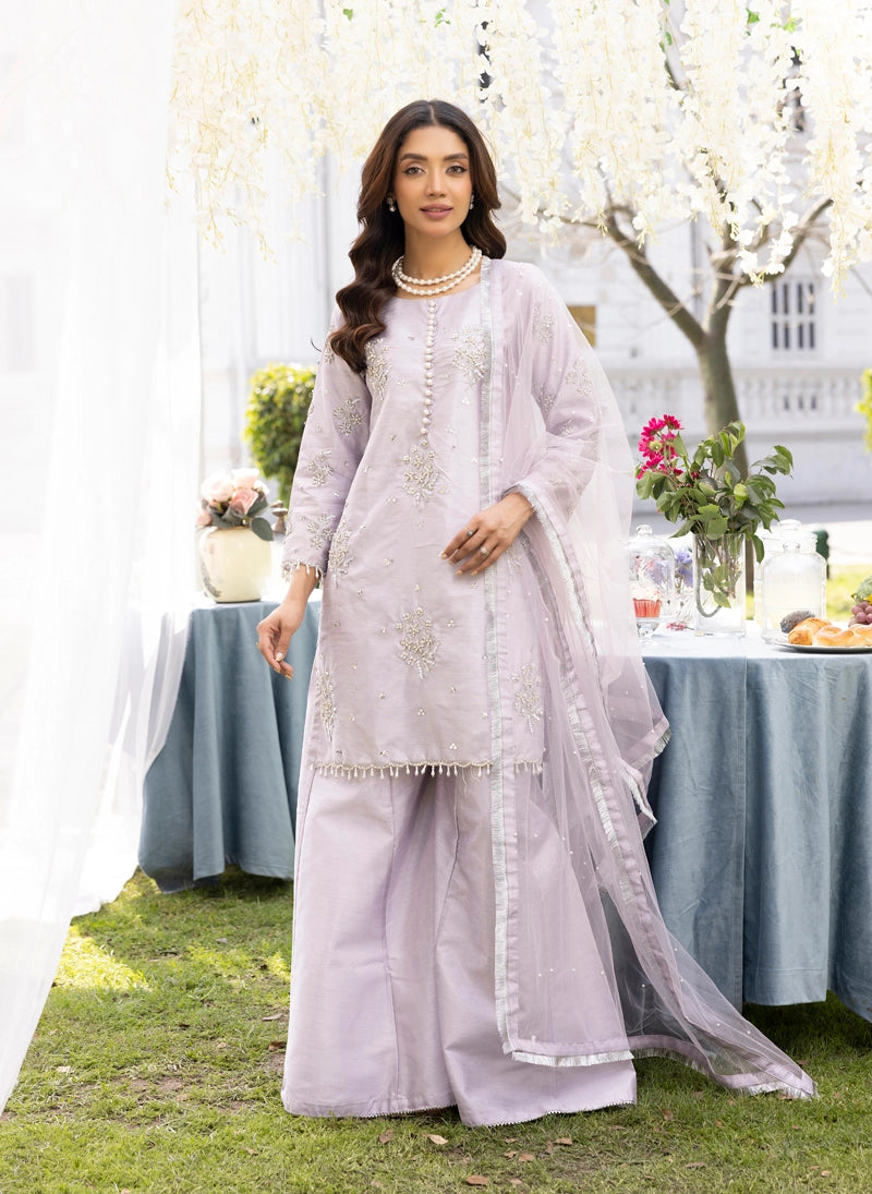 Woman in a light purple traditional outfit standing outdoors with a table and flowers in the background
