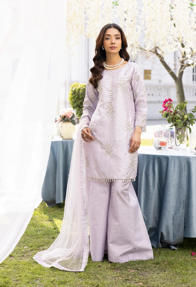 Woman in a light purple traditional outfit standing outdoors with a table and flowers in the background