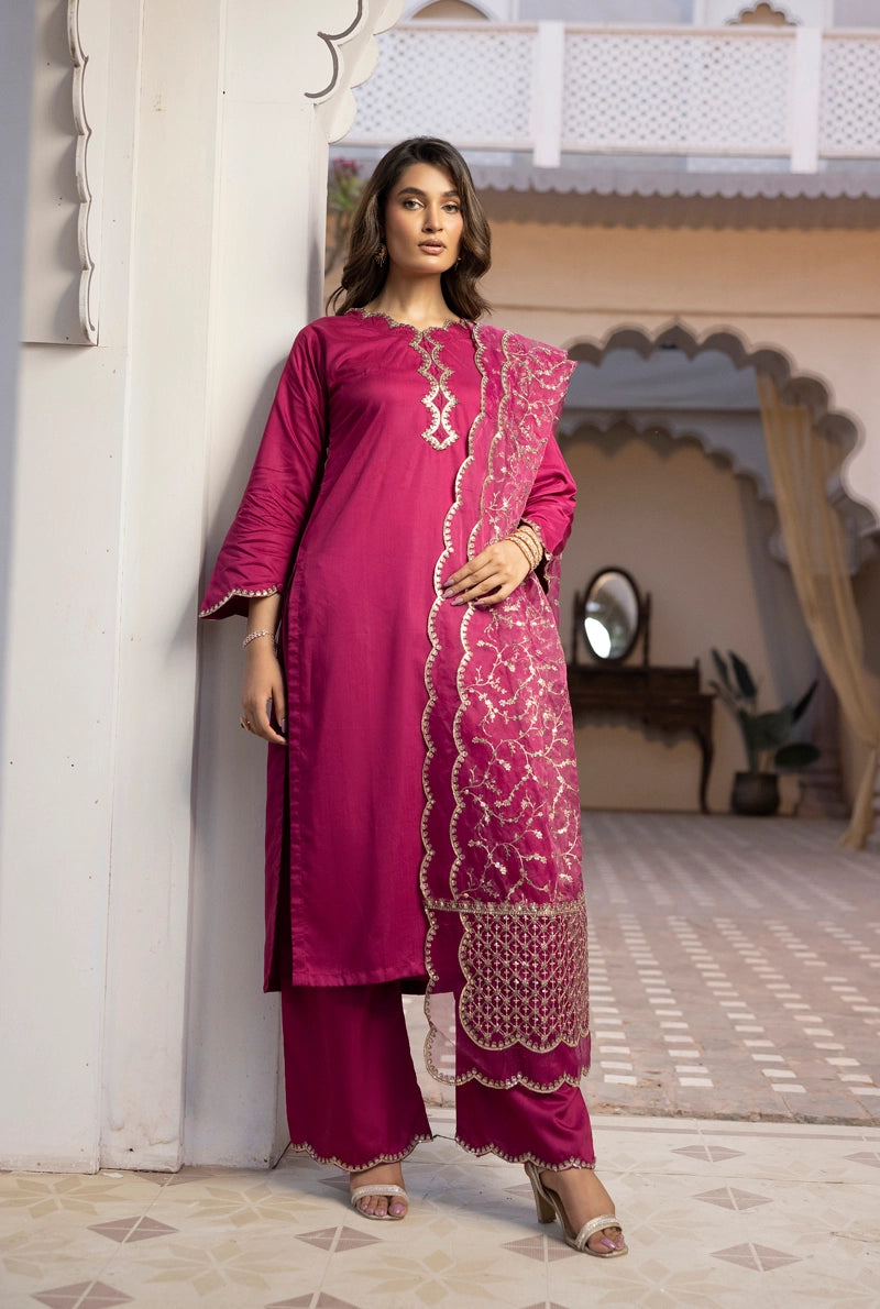 Woman in a pink traditional outfit standing in a decorative interior setting.