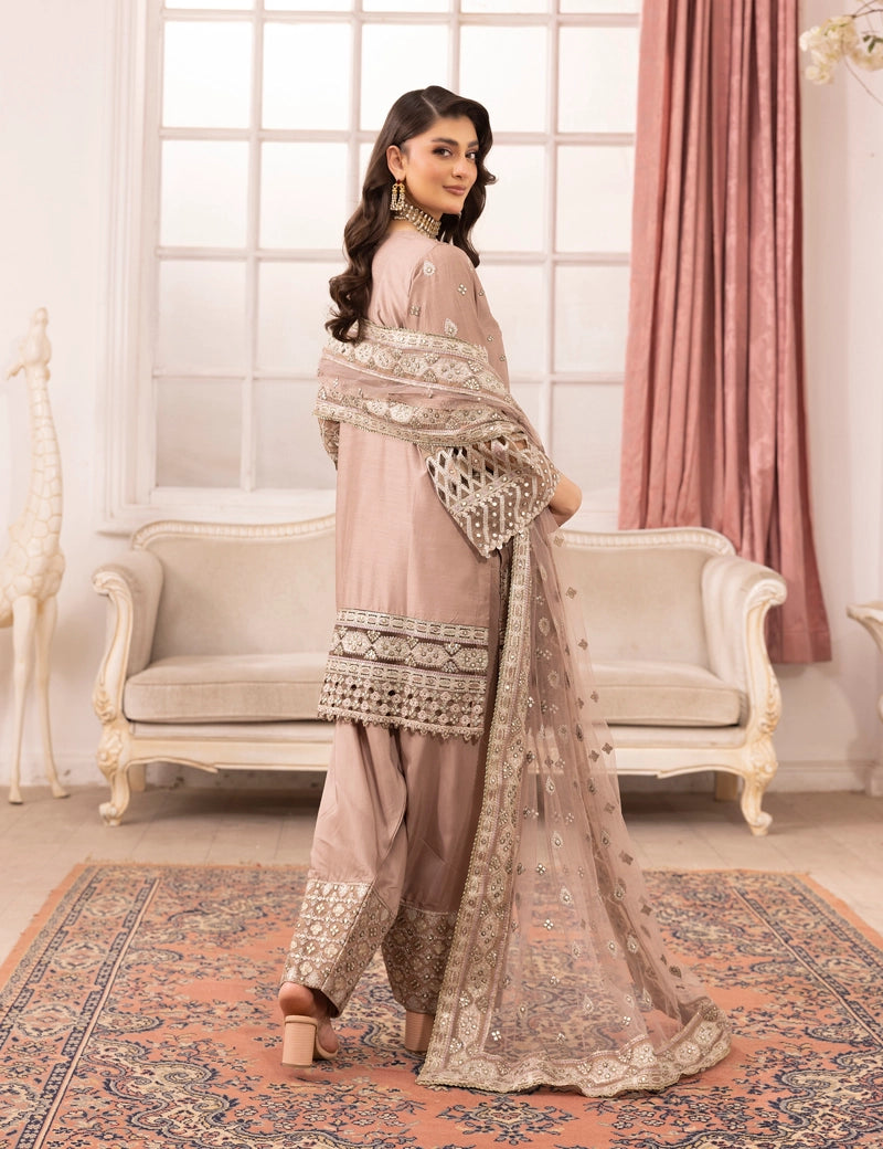 Woman in traditional pink embroidered outfit standing in a decorated room with pink curtains and a sofa.