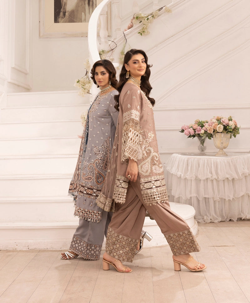 Two women in traditional outfits standing in a decorated room with flowers and a table.