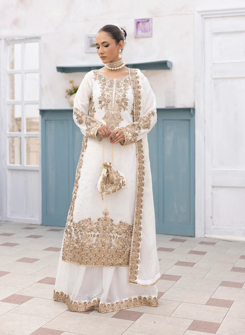 Woman in a white and gold embroidered traditional outfit standing in a room with white walls and blue cabinets.