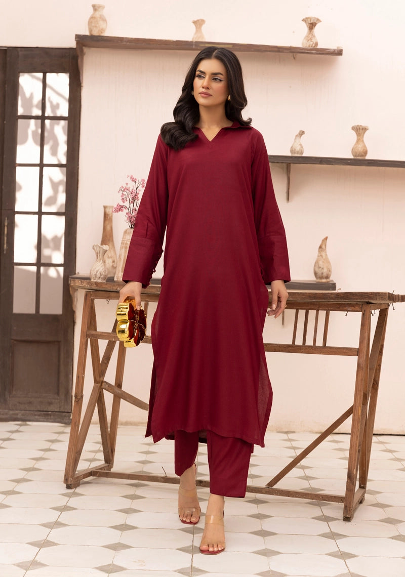 Woman in a maroon traditional outfit standing in a room with wooden furniture and decorative items.