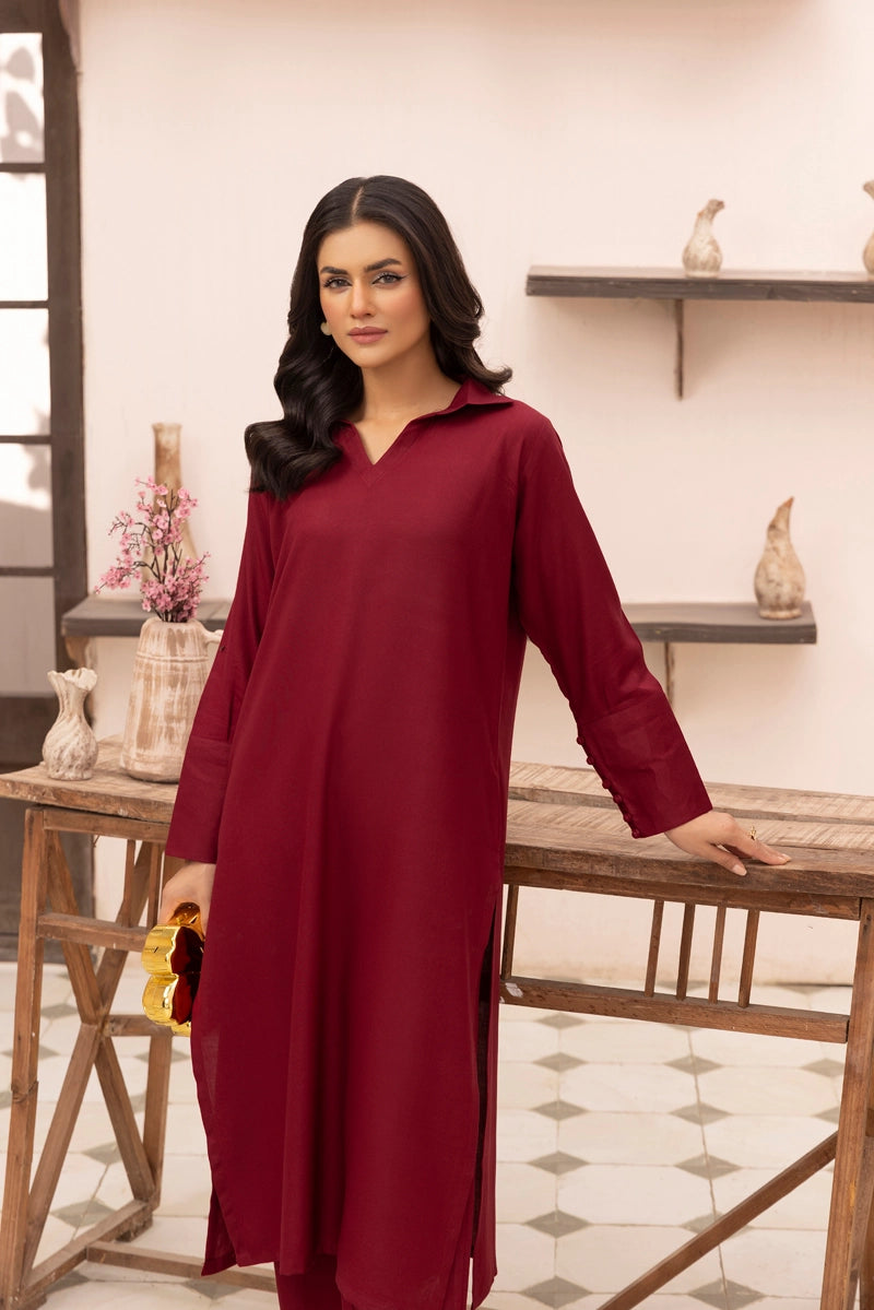 Woman wearing a red dress standing in a room with wooden furniture and decorative items.