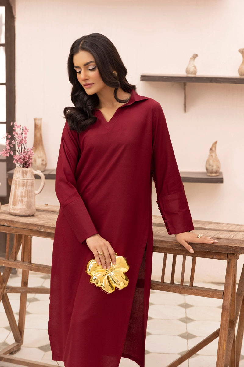Woman in a burgundy dress holding a gold clutch in an indoor setting.