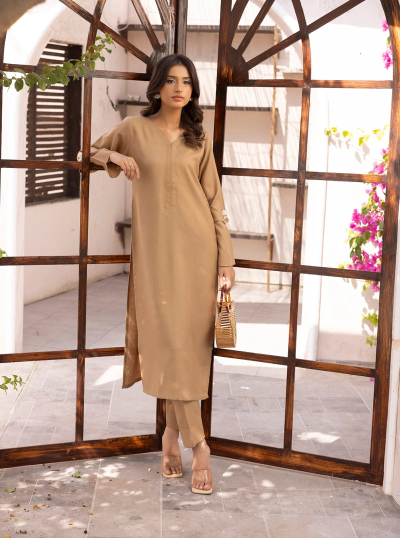 Woman in a beige outfit standing in front of a decorative wooden screen.