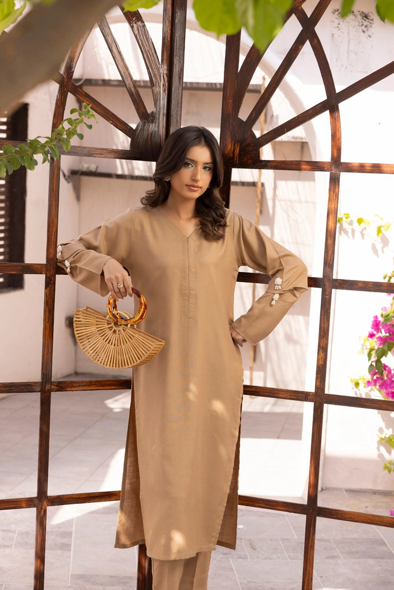 Woman in a beige outfit holding a fan-shaped handbag in front of a decorative metal screen.