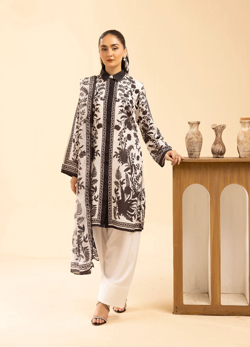 Woman wearing a black and white patterned kurta with white pants, standing next to a wooden cabinet with decorative vases.