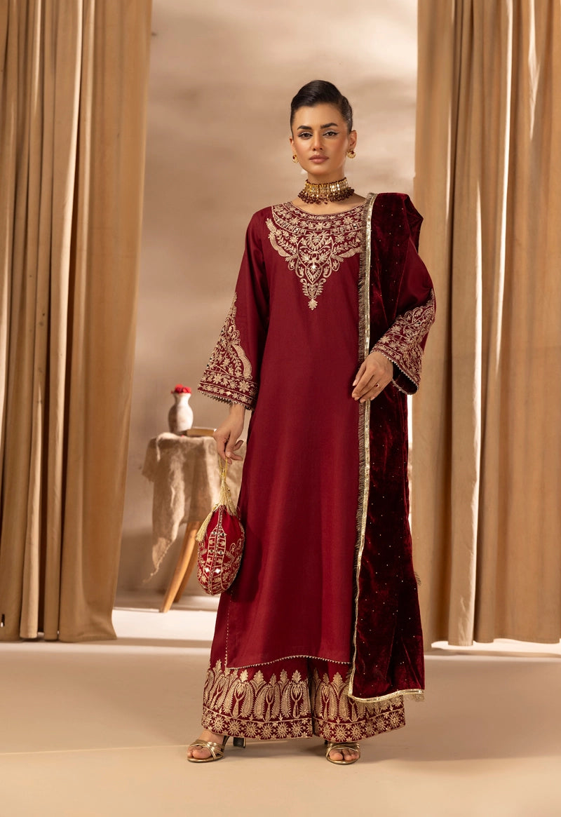Woman wearing a maroon traditional outfit with gold embroidery in a neutral setting.