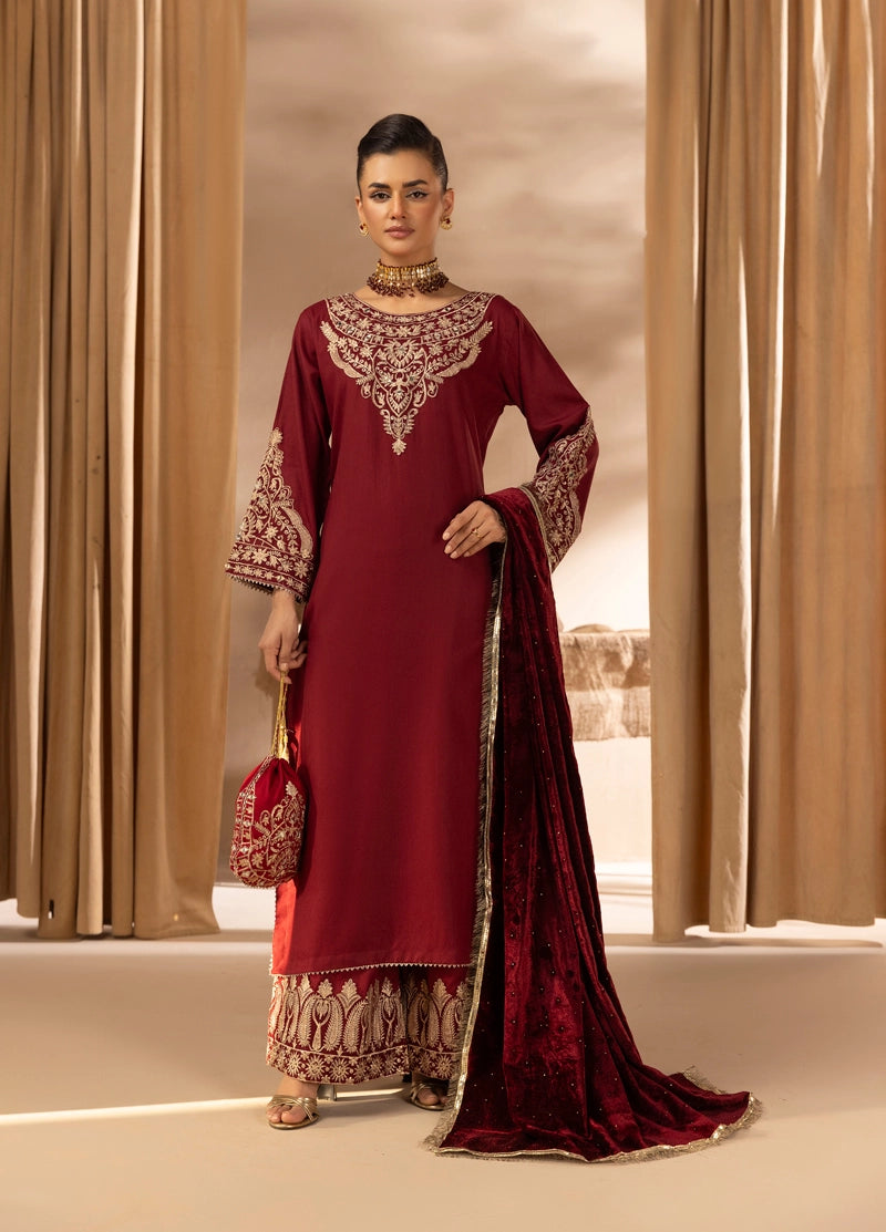 Woman in a maroon traditional outfit with intricate patterns standing against a neutral background.