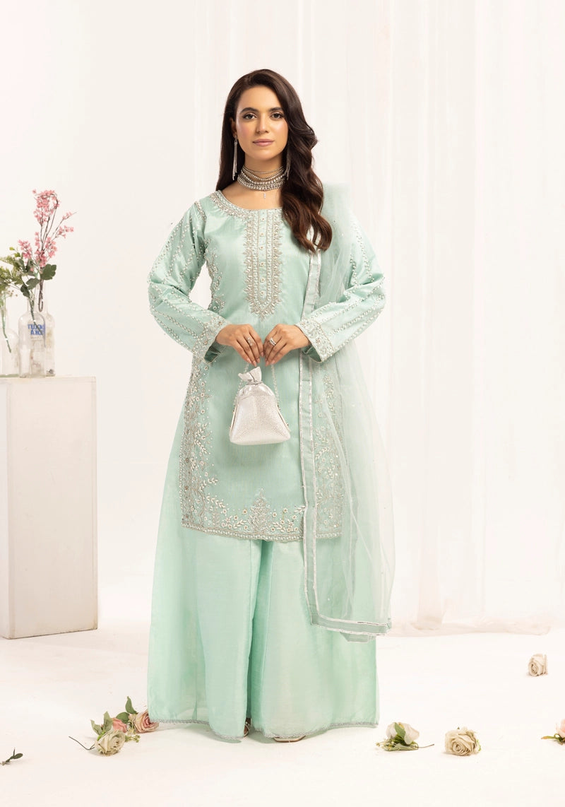 Woman wearing a light green traditional outfit with embroidery, standing against a white background.