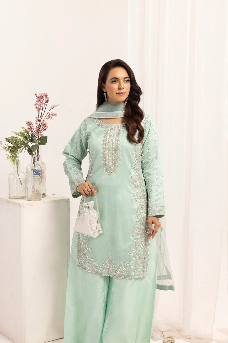 Woman wearing a light green traditional outfit with white embroidery in a bright room.