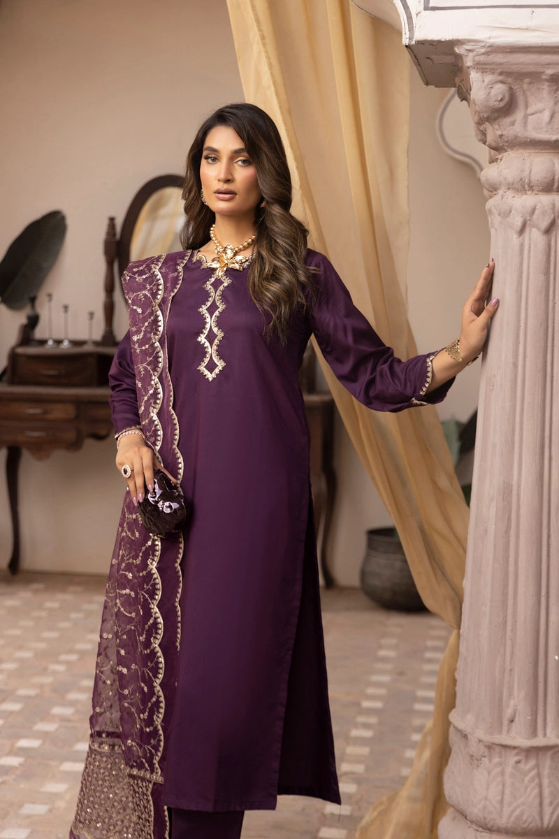Woman in a purple traditional outfit standing indoors with decor elements.