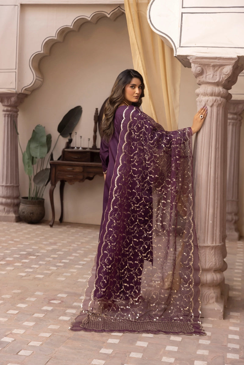 Woman in a purple traditional outfit standing in an ornate indoor setting.