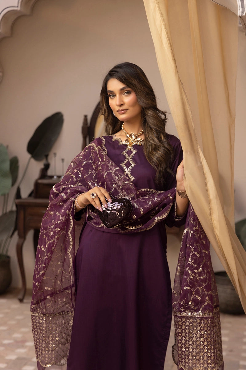 Woman in a purple traditional outfit with gold embroidery, standing indoors.