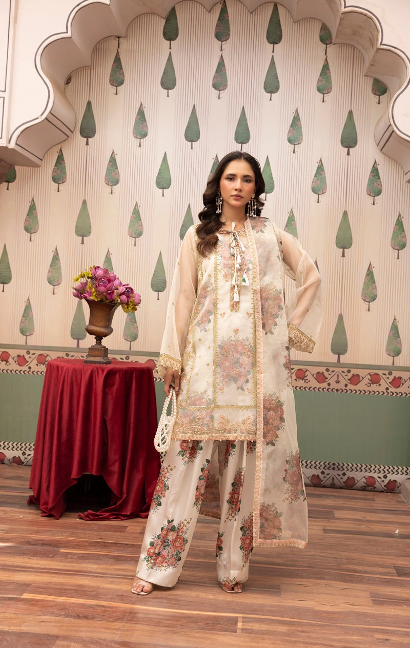 Woman in a floral outfit standing in front of a decorative wall with a table and flowers.