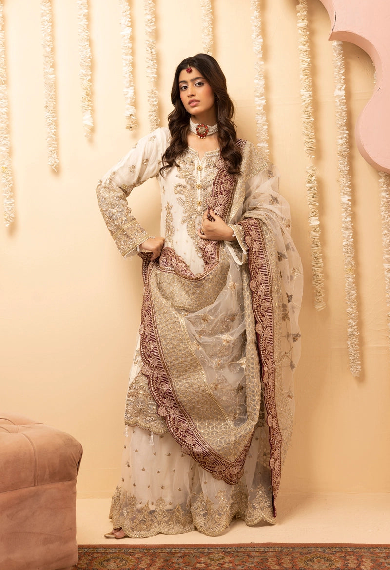 Woman in a traditional embroidered outfit standing against a decorative wall.