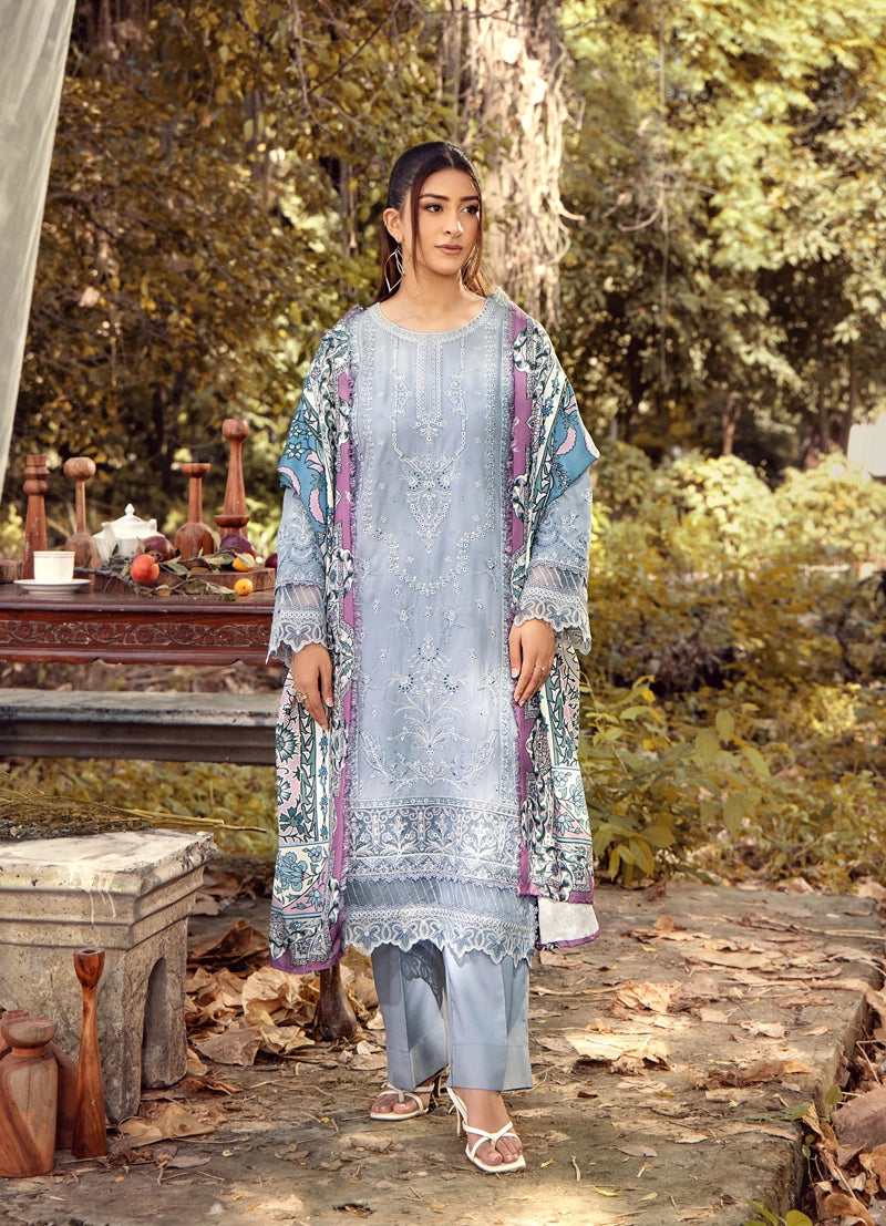 Woman in a light blue embroidered outfit standing in a natural setting with trees and a path.