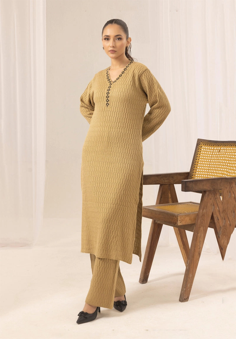 Woman wearing a mustard yellow outfit standing next to a wooden chair with a woven backrest.