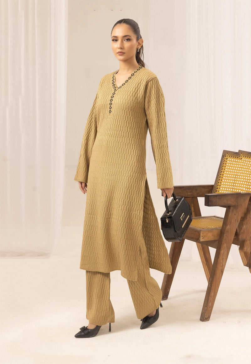 Woman in a beige outfit standing next to a wooden table with a chair.