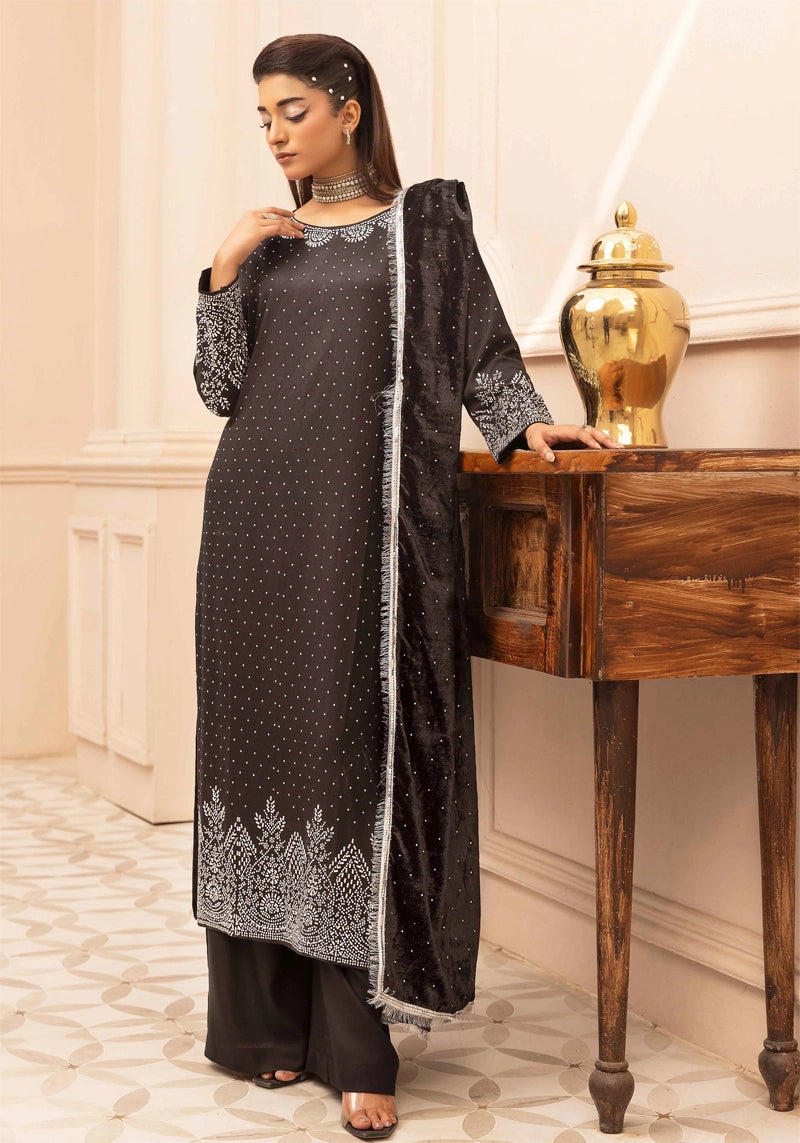 Woman in a black and silver traditional outfit standing in a room with a wooden table and decorative items.