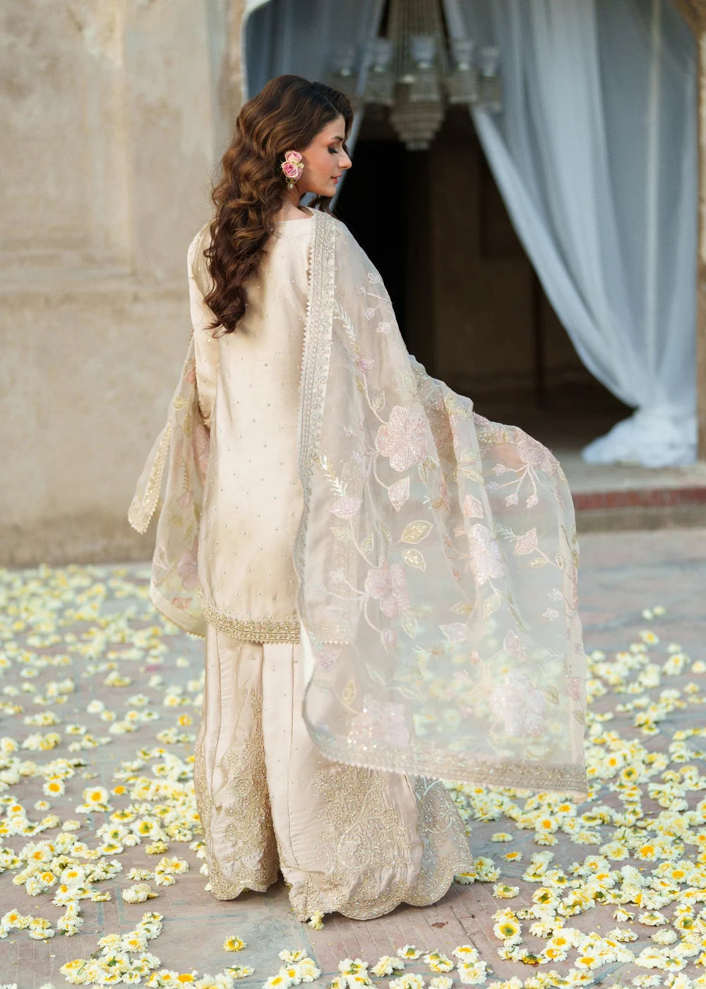 Woman in a traditional white outfit with floral patterns standing on a path with flowers.