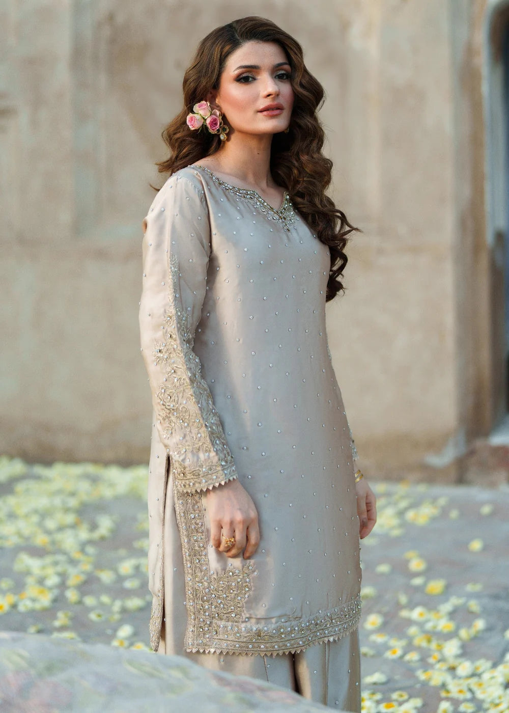 Woman in a light gray traditional outfit with floral earrings against a neutral background