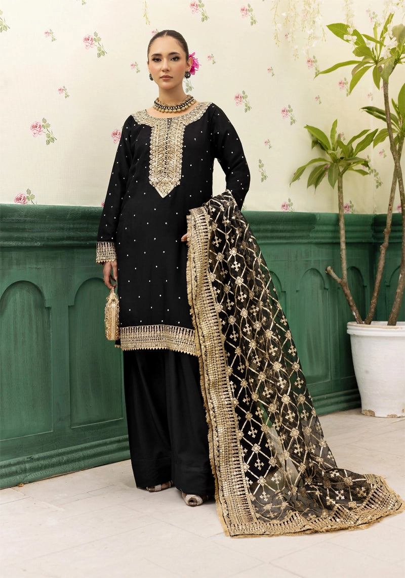 Woman in traditional black and gold outfit with a decorative shawl against a floral wallpaper background.