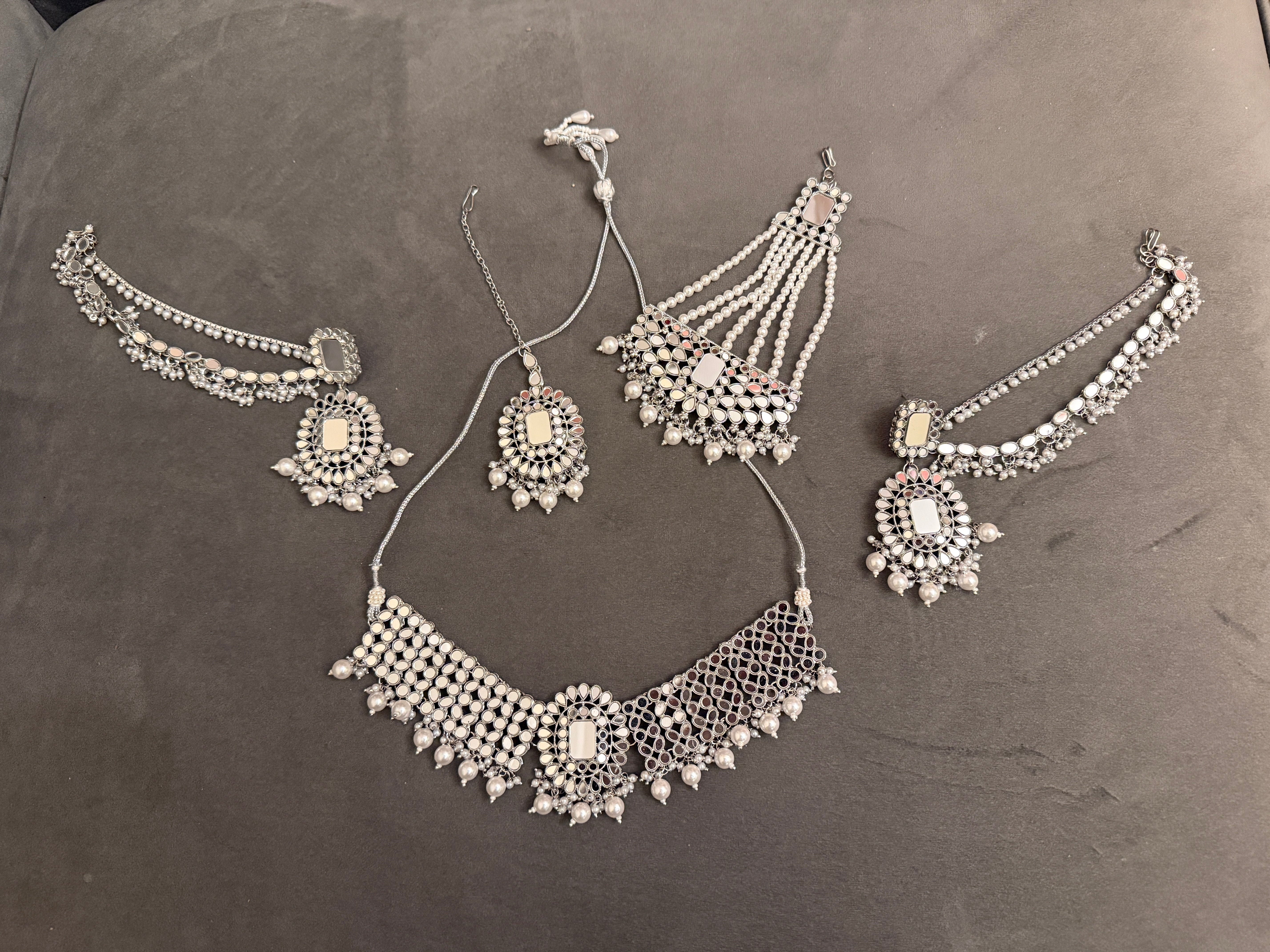 Silver jewelry set including choker necklace, earrings, tikka and chumbar on a gray background