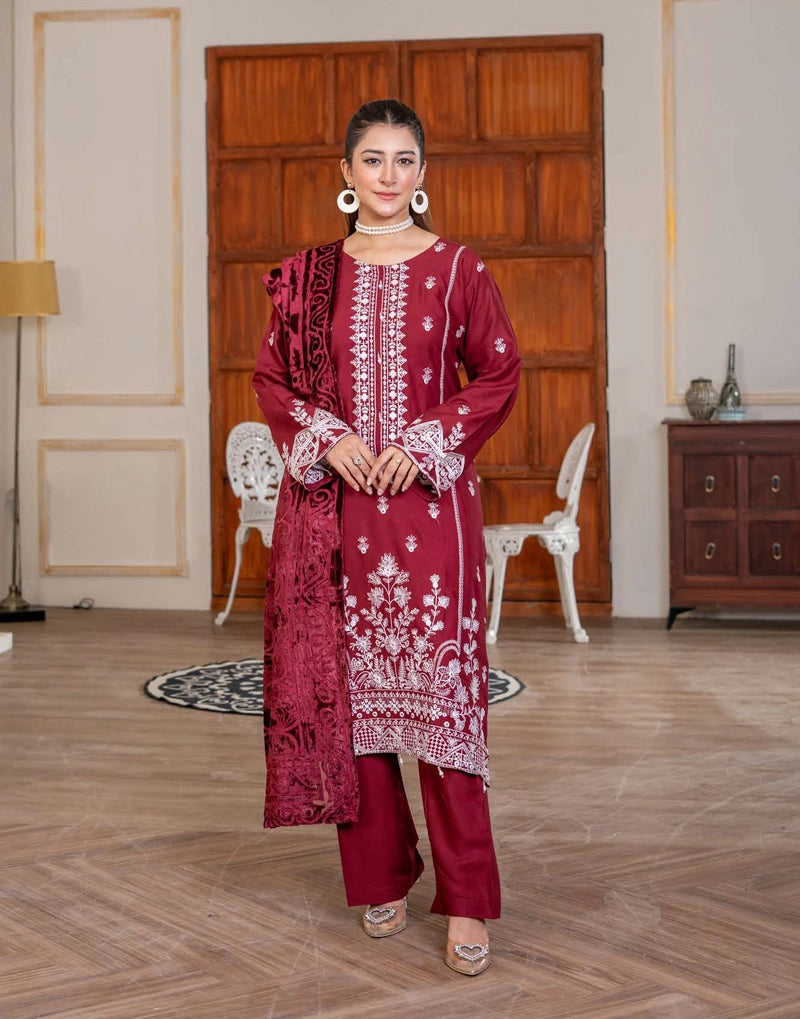 Woman in a maroon embroidered outfit standing in a room with wooden floor and furniture.