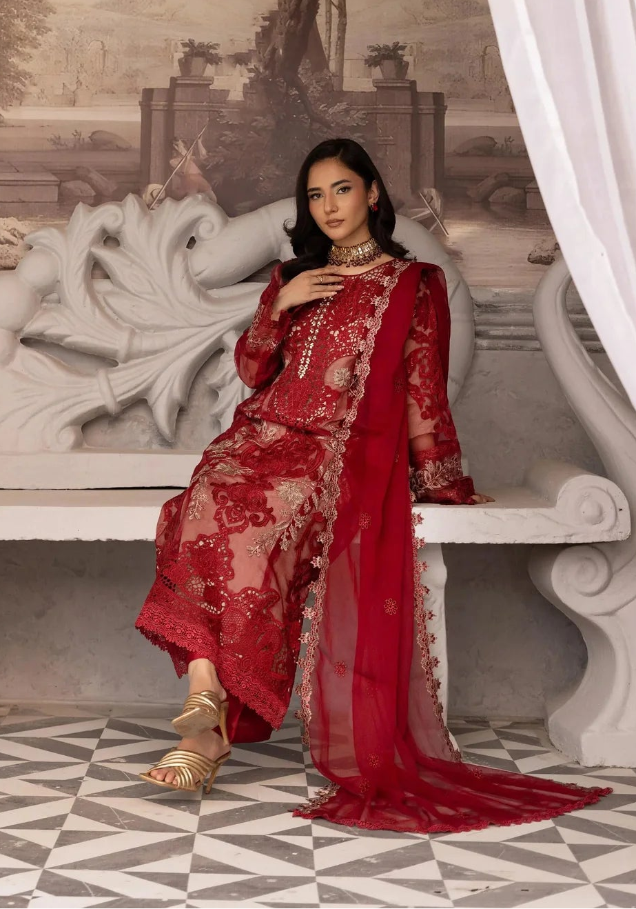 Woman in a red embroidered outfit sitting on a decorative chair with classical architecture in the background.