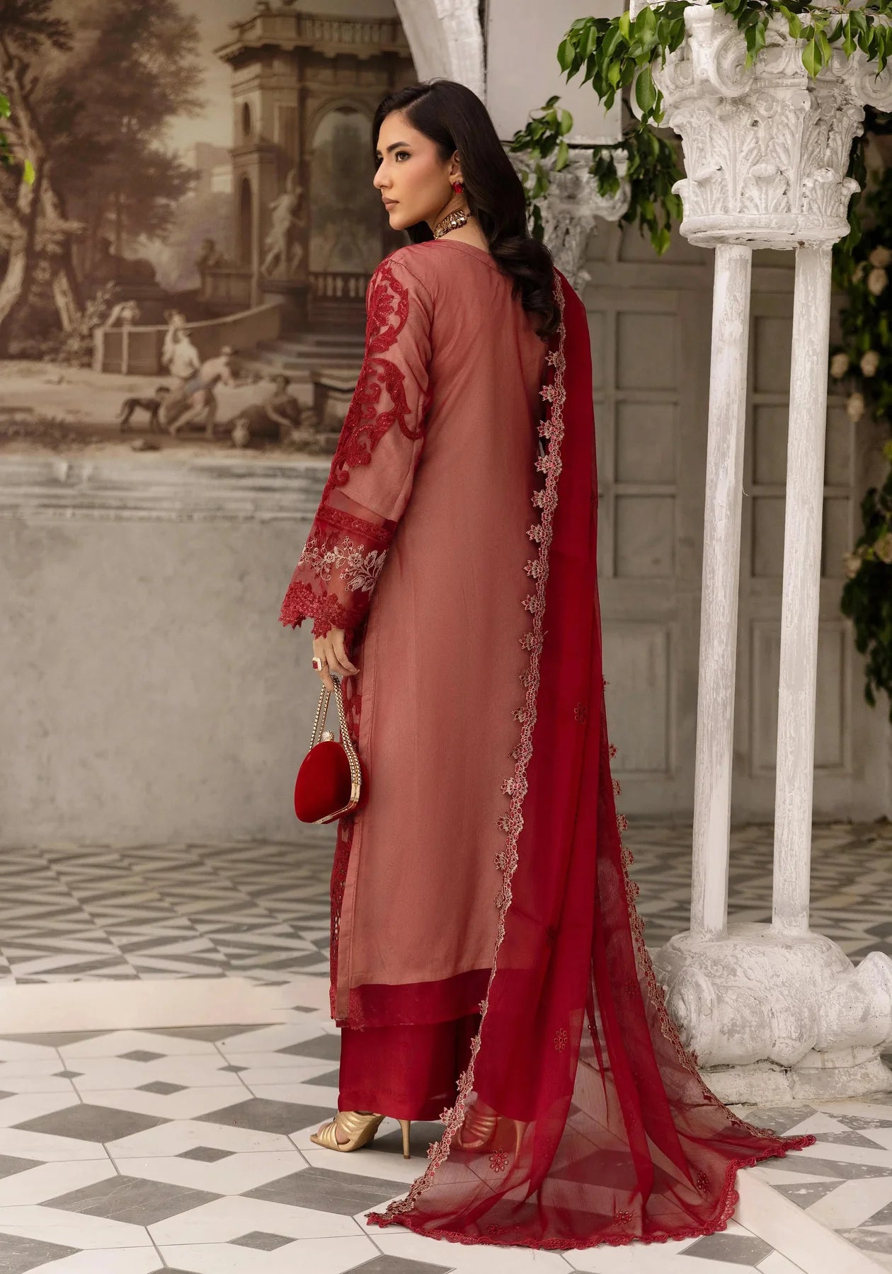 Woman in a red and pink traditional outfit standing in an elegant indoor setting.