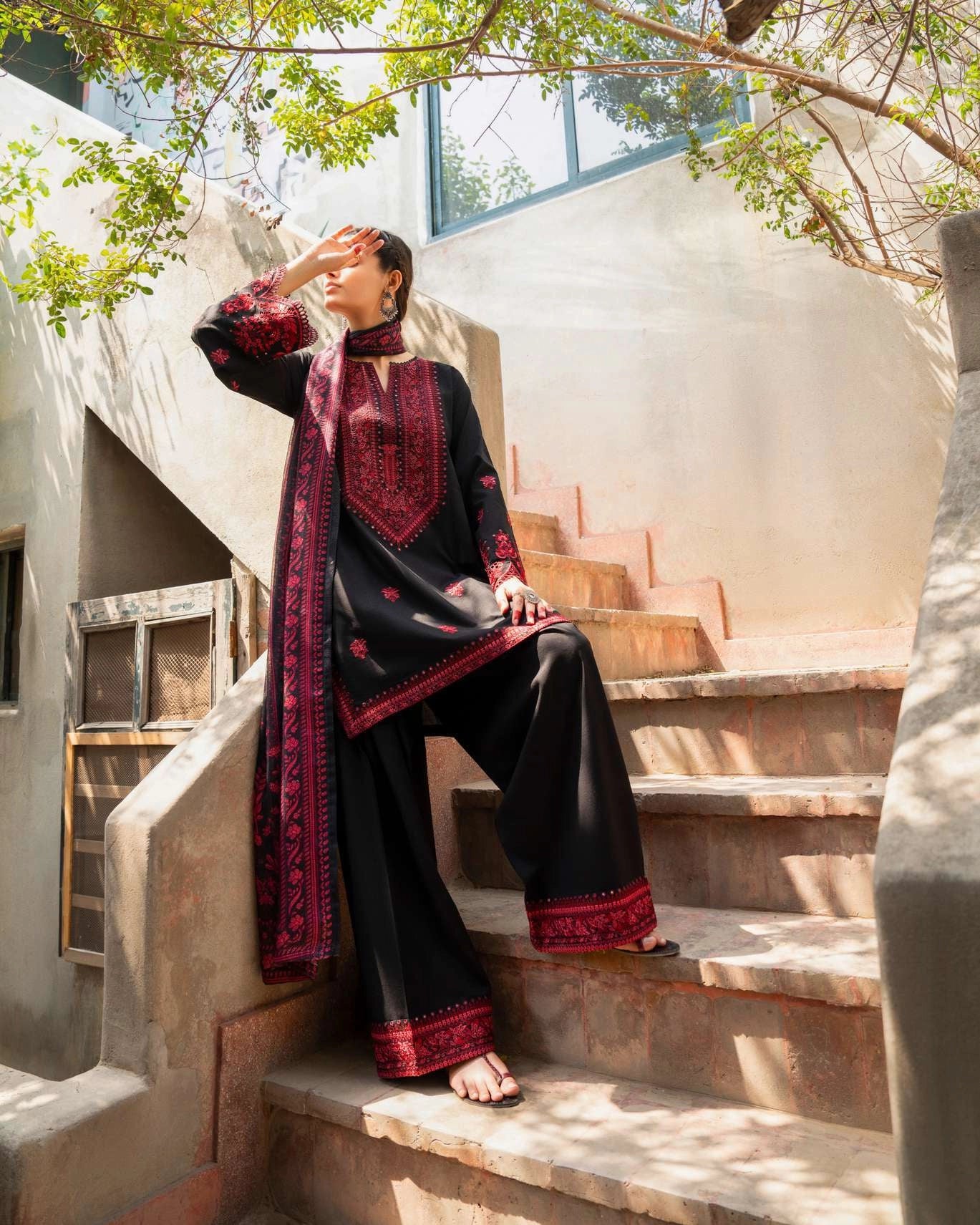 Woman in traditional black and red outfit sitting on stone steps outdoors