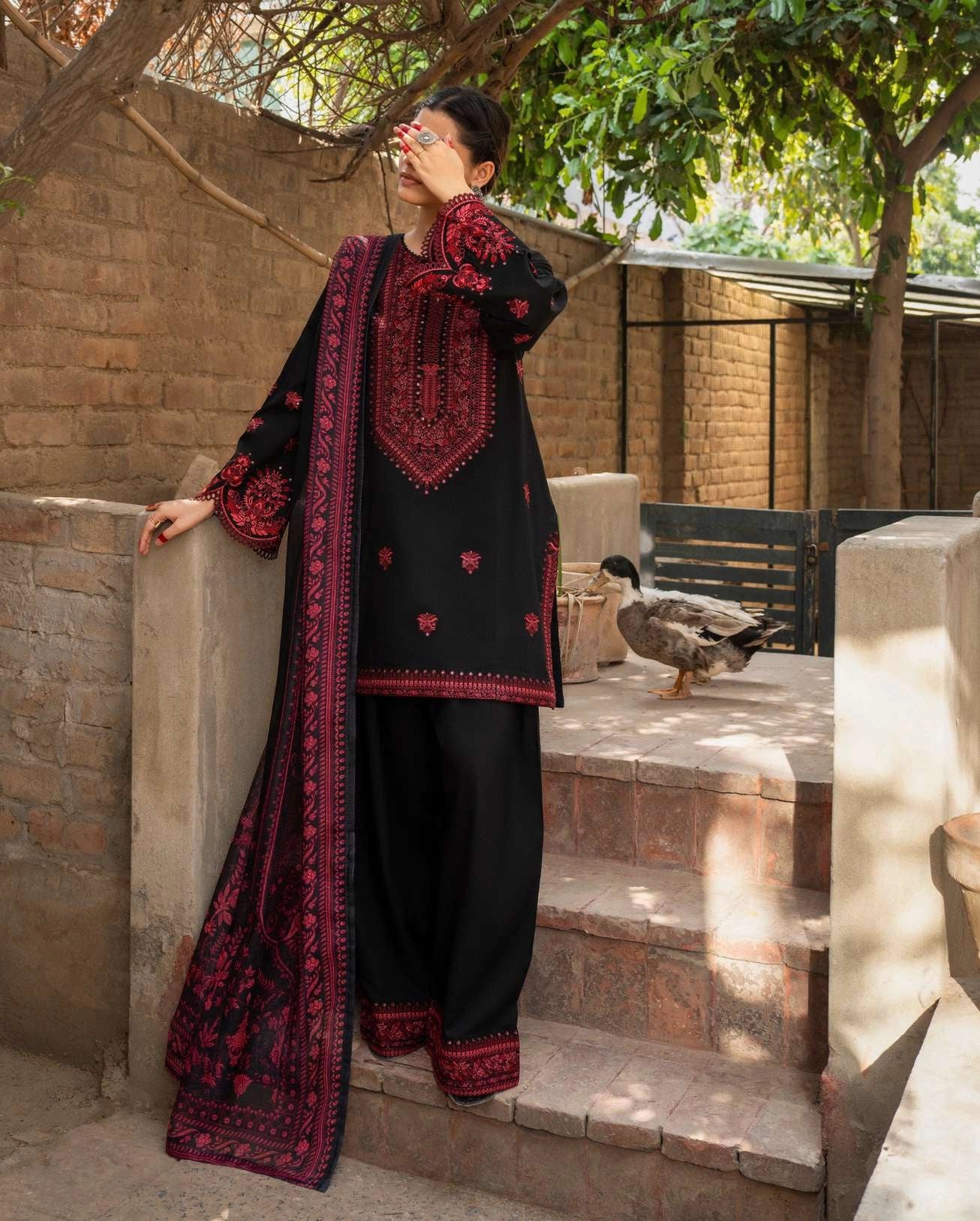 Woman wearing a black and red traditional outfit standing on stone steps with a duck in the background.